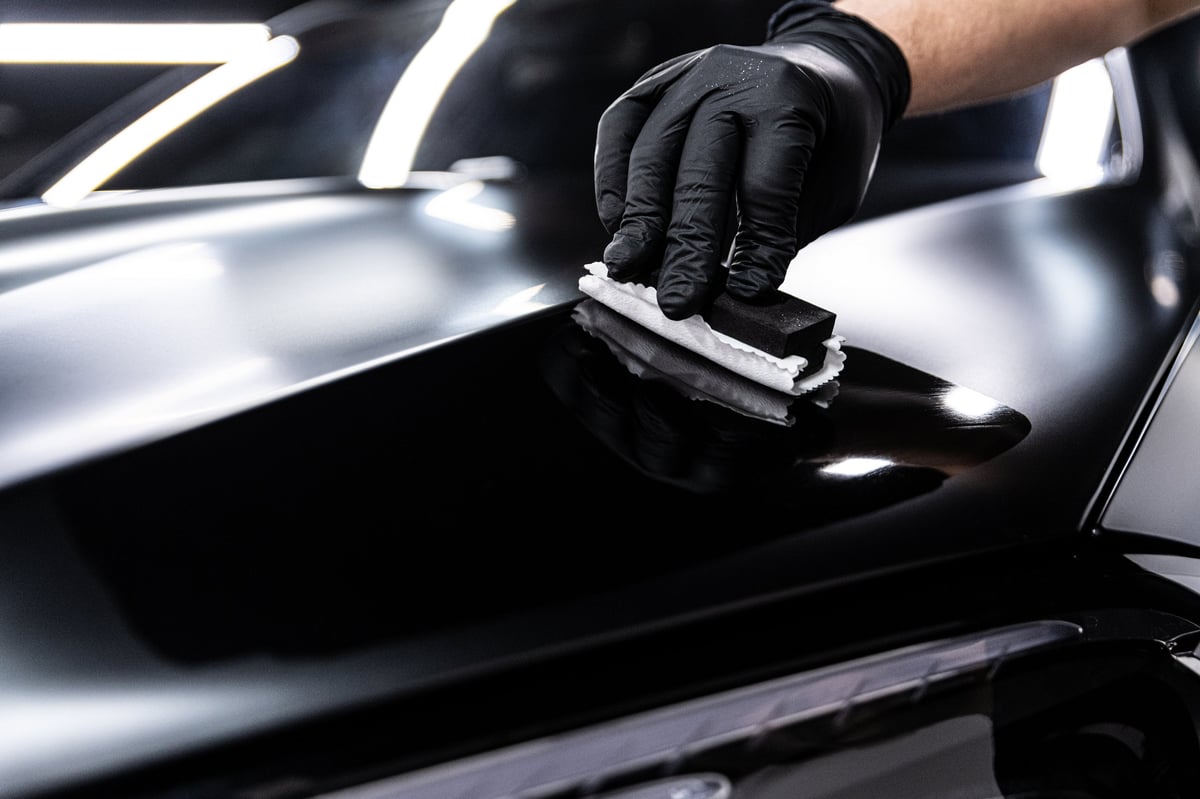 Detailer applying ceramic coating to black paint for deep gloss and protection